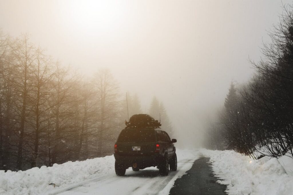 SUV travels on a snow-covered road through a foggy winter forest. Serene and scenic travel scene.